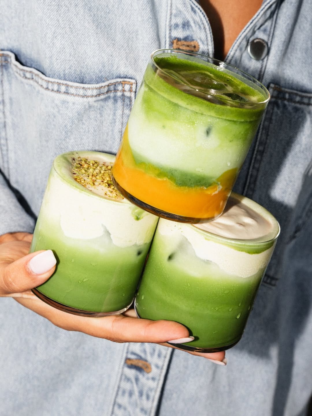Stacked iced matcha and yuzu drinks held up in SANI cups