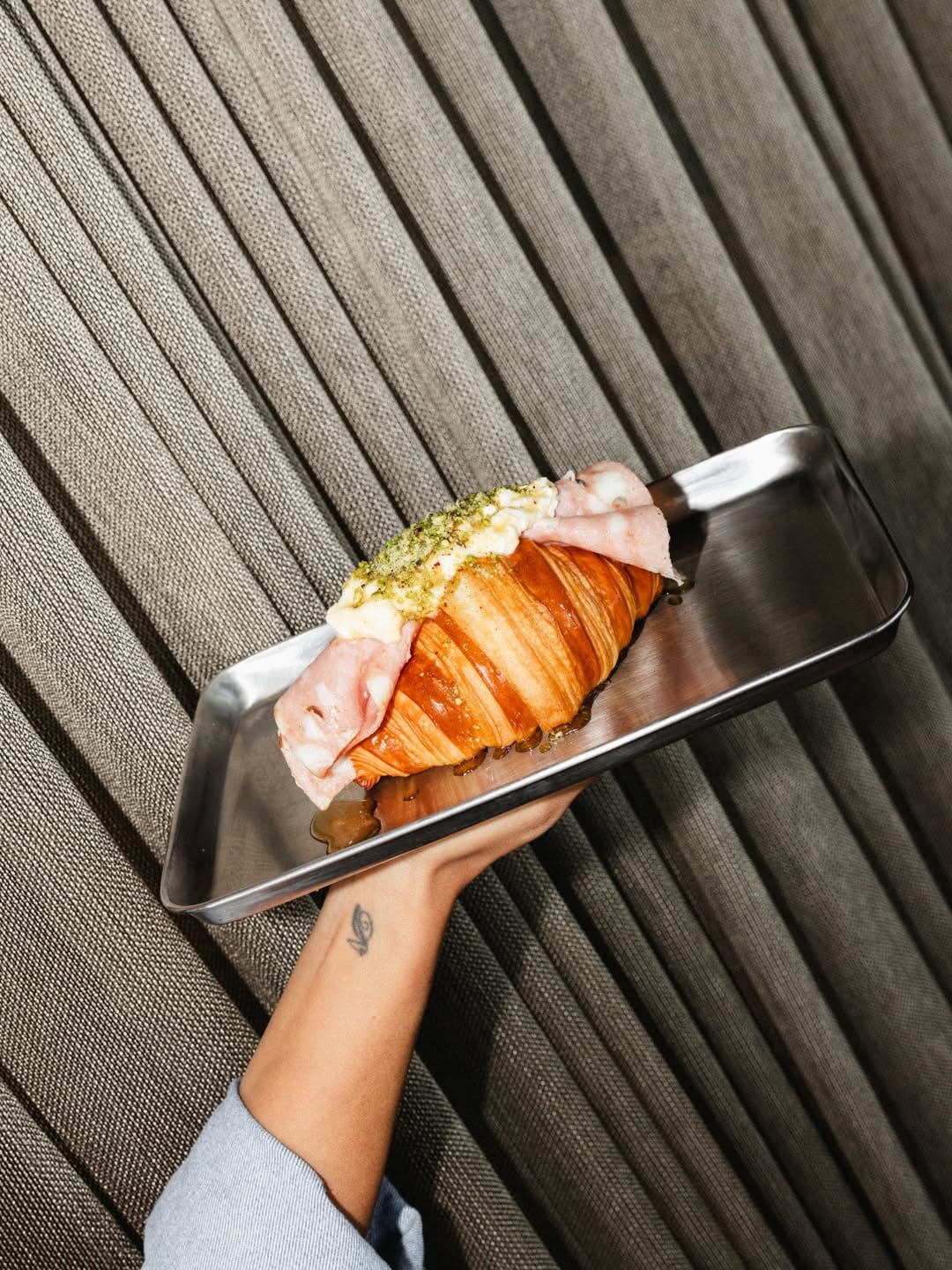 Mortadella, stracciatella, pistachio and honey croissant on a steel tray