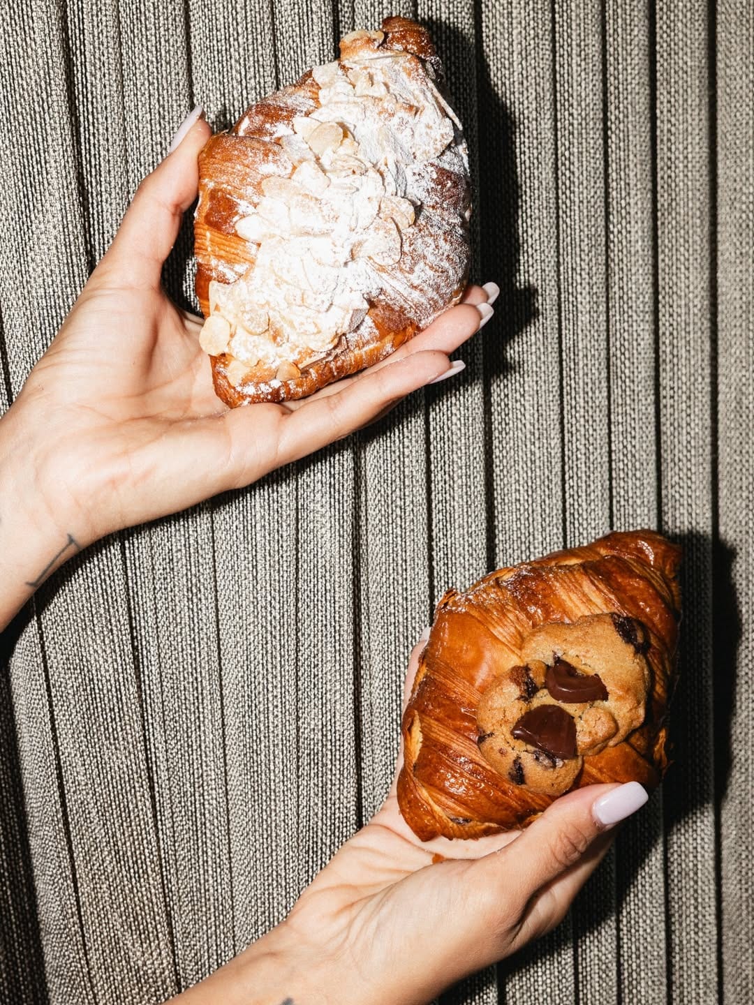 Hands holding an almond croissant and a chocolate croissant