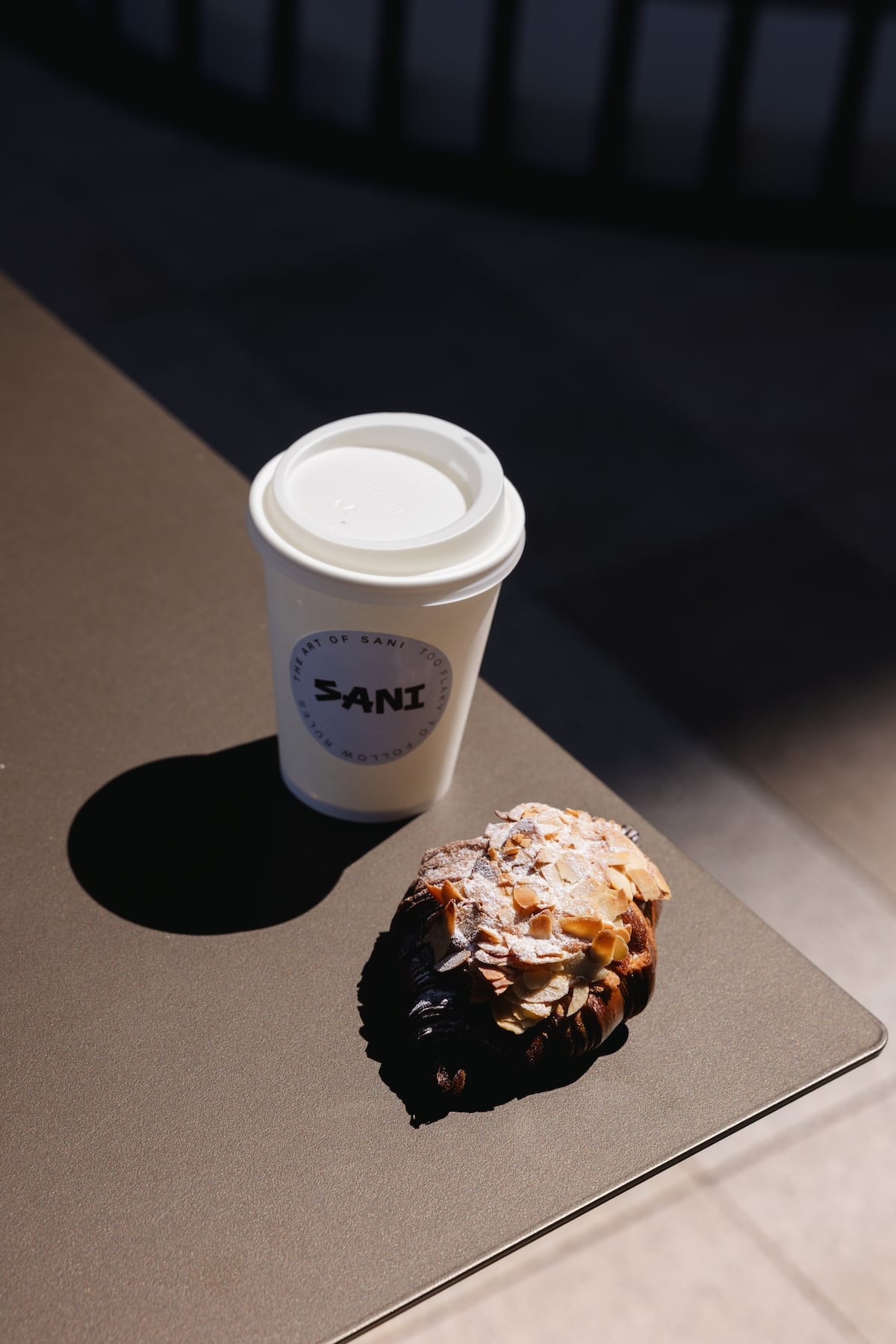 SANI branded coffee cup beside an almond croissant